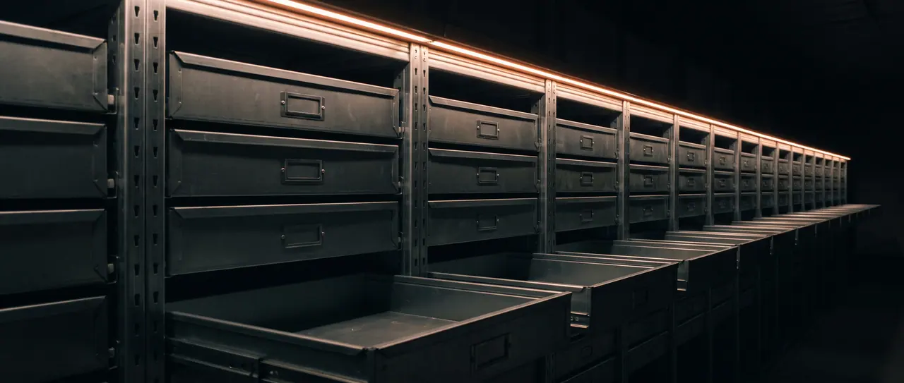 A long row of flat steel drawers in an archive rack, all pulled out equally far, their front edges forming a continuous line into the depth.