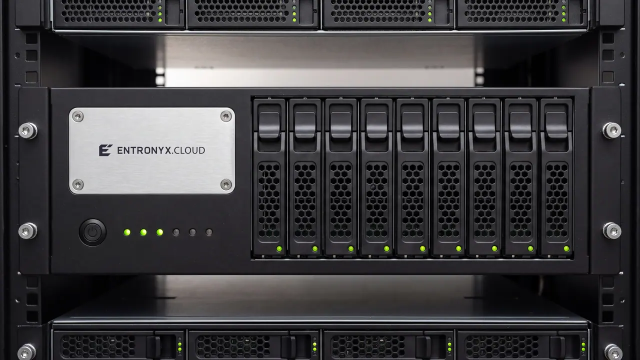 Die Front eines schwarzen 2-HE-Servers im Rack, frontal aufgenommen: links auf der matten Blende eine Plakette aus gebürstetem Aluminium mit der eingravierten Aufschrift ENTRONYX CLOUD und einer Schraube in jeder Ecke, darunter ein runder Einschalttaster und eine Reihe kleiner Statuslichter, drei davon grün; rechts neun gleiche Laufwerksschlitten mit Kunststoffriegel, Sechskantlochung und je einem grünen Statuslicht. Darüber und darunter die Lochblechfronten der Nachbarserver, links und rechts die schwarzen Rackholme.