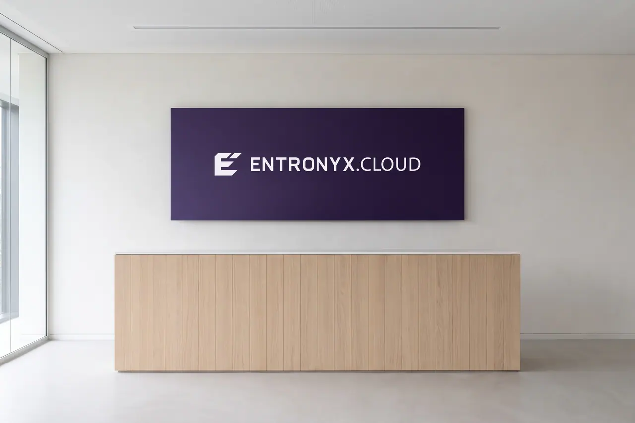 Illustration eines Empfangs: an einer weißen Wand eine dunkelviolette Tafel mit dem Zeichen und dem hellen Schriftzug ENTRONYX.CLOUD, davor ein Empfangstresen aus heller Eiche, links eine Glaswand.