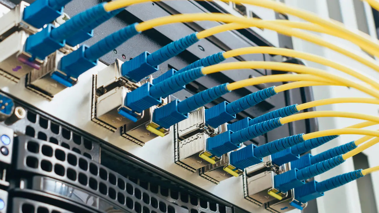 Gelbe Glasfaserkabel mit blauen Steckern, gesteckt in eine Reihe von Transceivern an der Rückseite eines Servers.