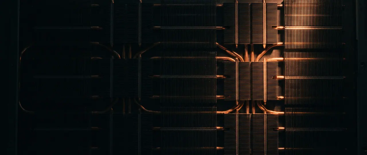 Rows of milled cooling fins in strict alignment, photographed vertically from above, bare copper heat pipes across them, a narrow warm streak of light on the right edge.